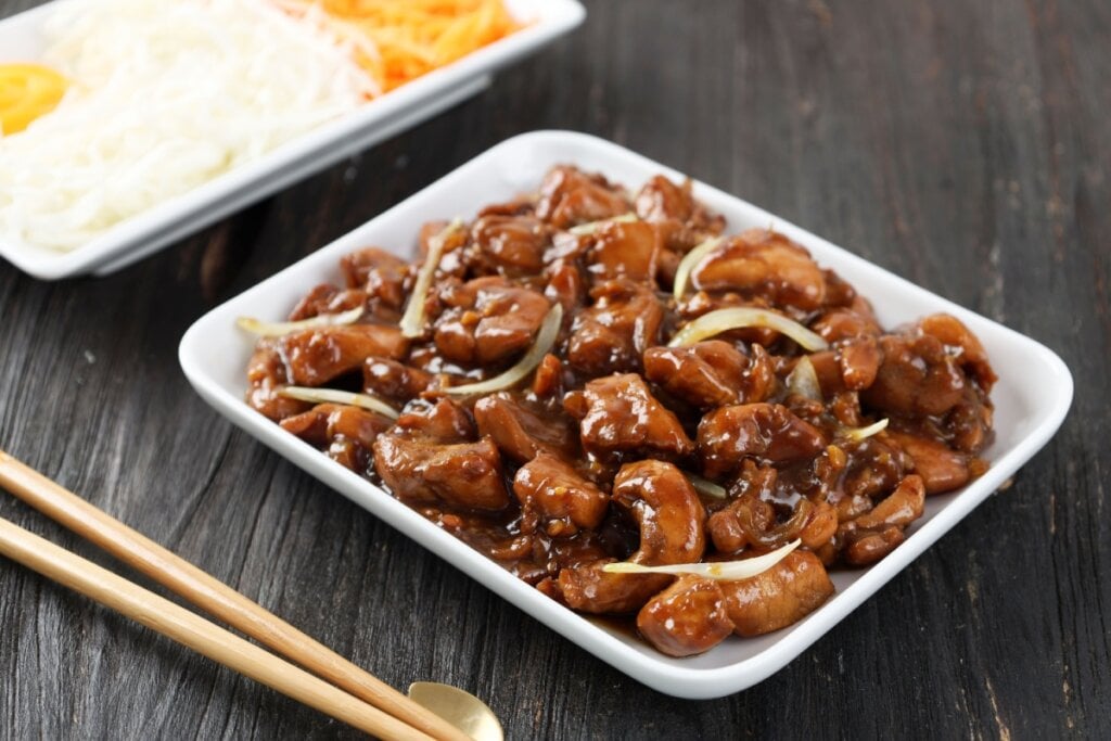 Frango teriyaki ao estilo brasileiro em recipiente branco; ao lado, hashis