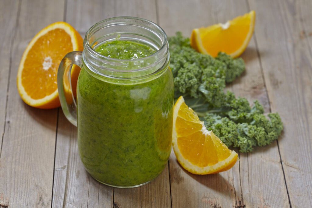 Copo de vidro com suco de laranja com alface em cima de uma mesa de madeira 