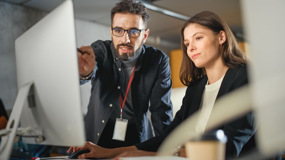 Homem mostrando para uma mulher algo na tela do computador