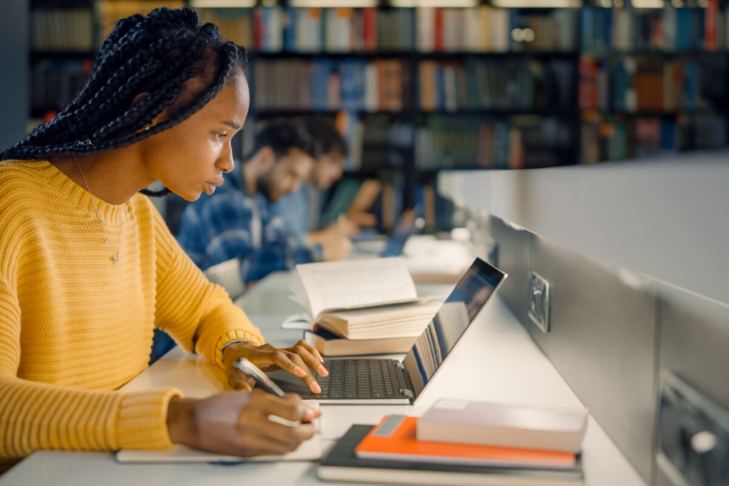 menina em espaço com livros usando notebook e escrevendo em papel