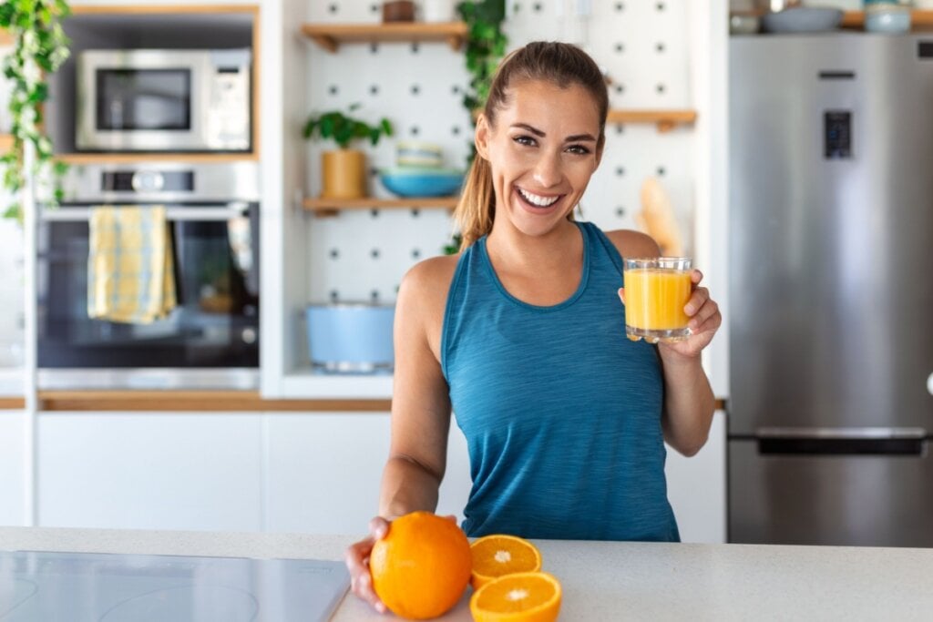 mulher bebendo suco de laranja segurando laranja em cozinha