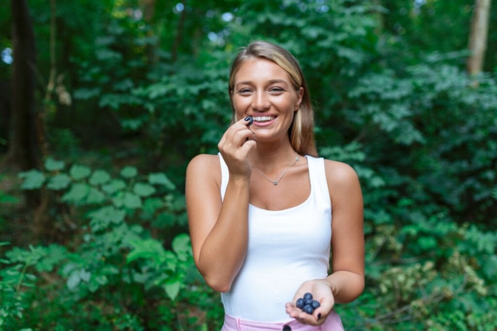 Mulher comendo mirtilo e com mirtilos na mão