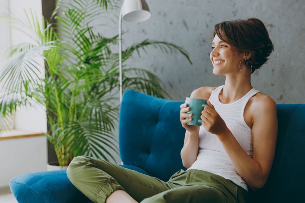 Mulher bebendo chá sentada em sofá sorrindo