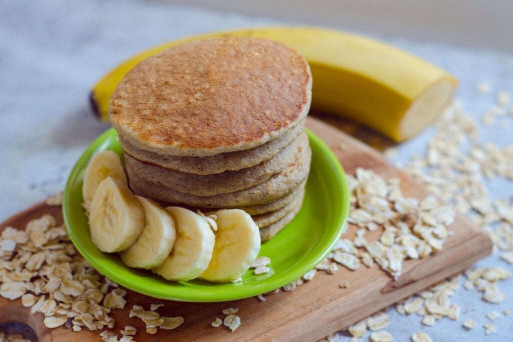 Panqueca de banana com aveia servidas em um prato verde em cima de uma tábua de madeira