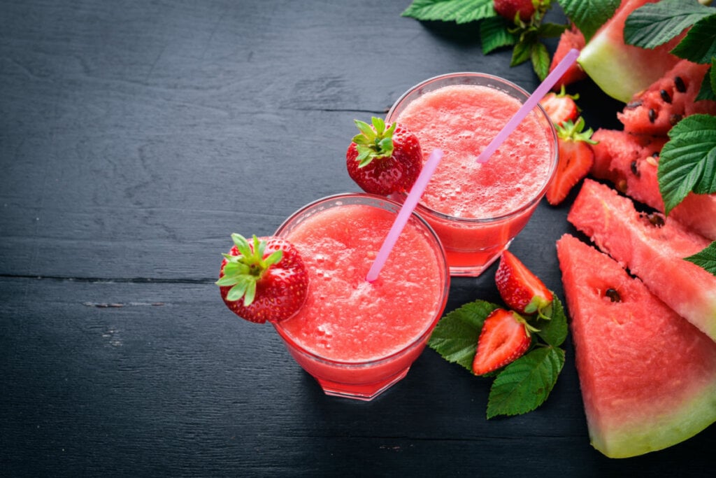 Um copo de suco com morangos e pedaços de melancia ao redor