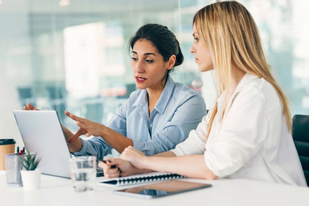 Duas mulheres sentadas em uma sala de reunião e olhando para um notebook