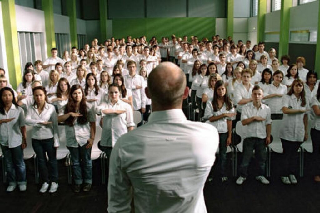 Homem em um palco e alunos em baixo o imitando no filme " A Onda"