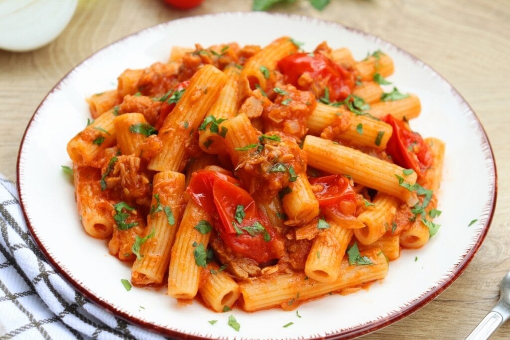 Prato branco com macarrão, molho de tomate, pedaços de tomate e atum polvilhados com coentro picado