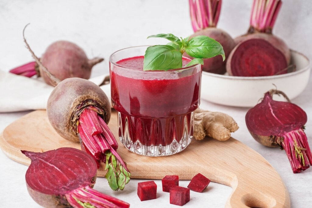 Suco de beterraba com gengibre em um copo de vidro em cima de uma tábua de madeira com pedaços de beterraba e gengibre 