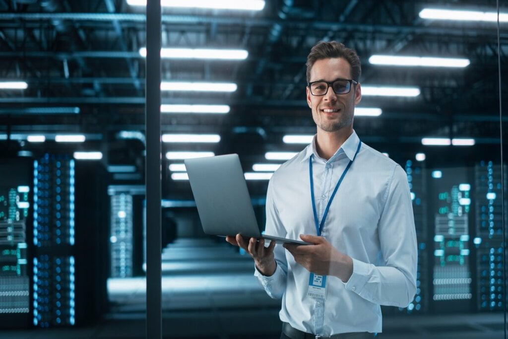 Homem com camisa social branca usando óculos preto e segurando um notebook