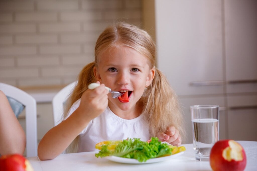 criança comendo salada sentada em mesa com cadeira