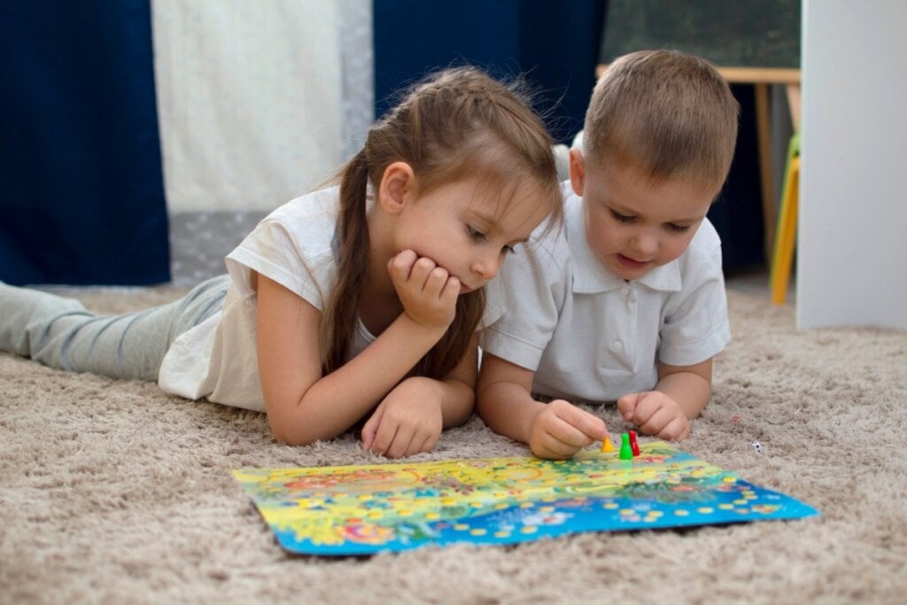 Duas crianças deitadas em tapete brincando com jogo de tabuleiro