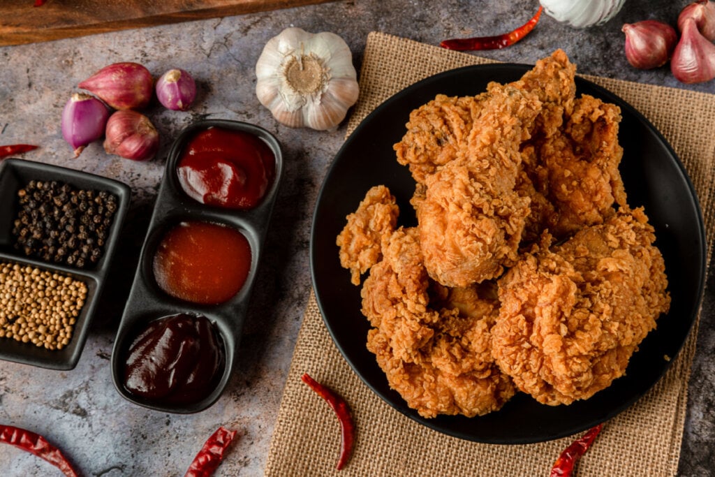 Pedaços de frango frito em prato preto e recipientes com molho ao lado 