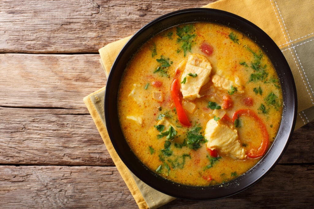 Moqueca de peixe com caldo, pimentão vermelho e coentro em recipiente preto