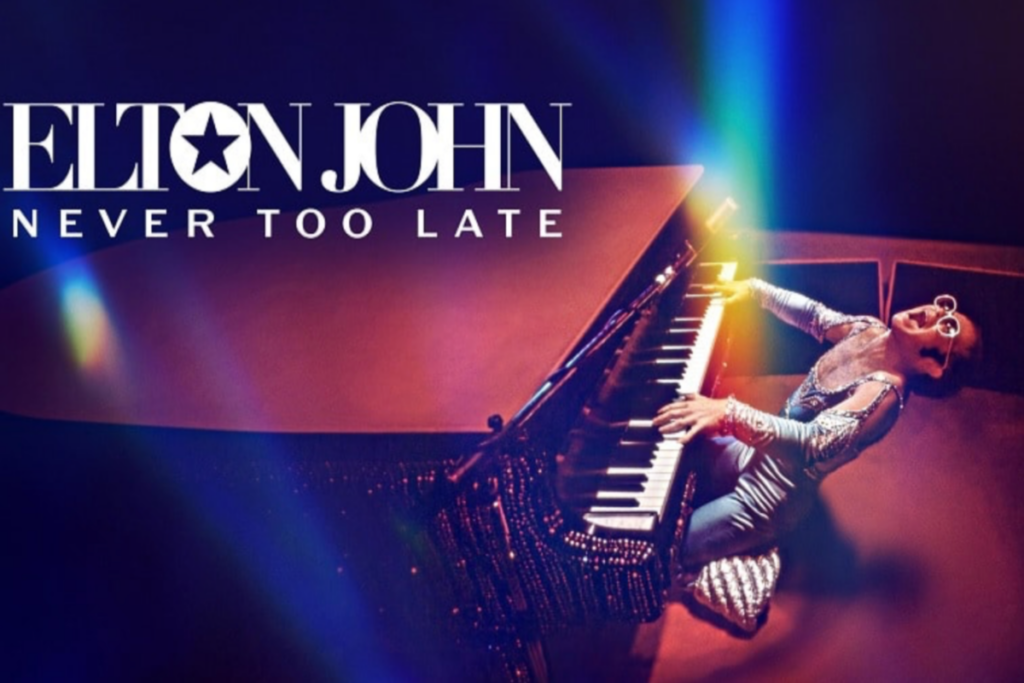 Imagem de Elton John tocando piano com um traje brilhante, em um cenário vibrante e iluminado