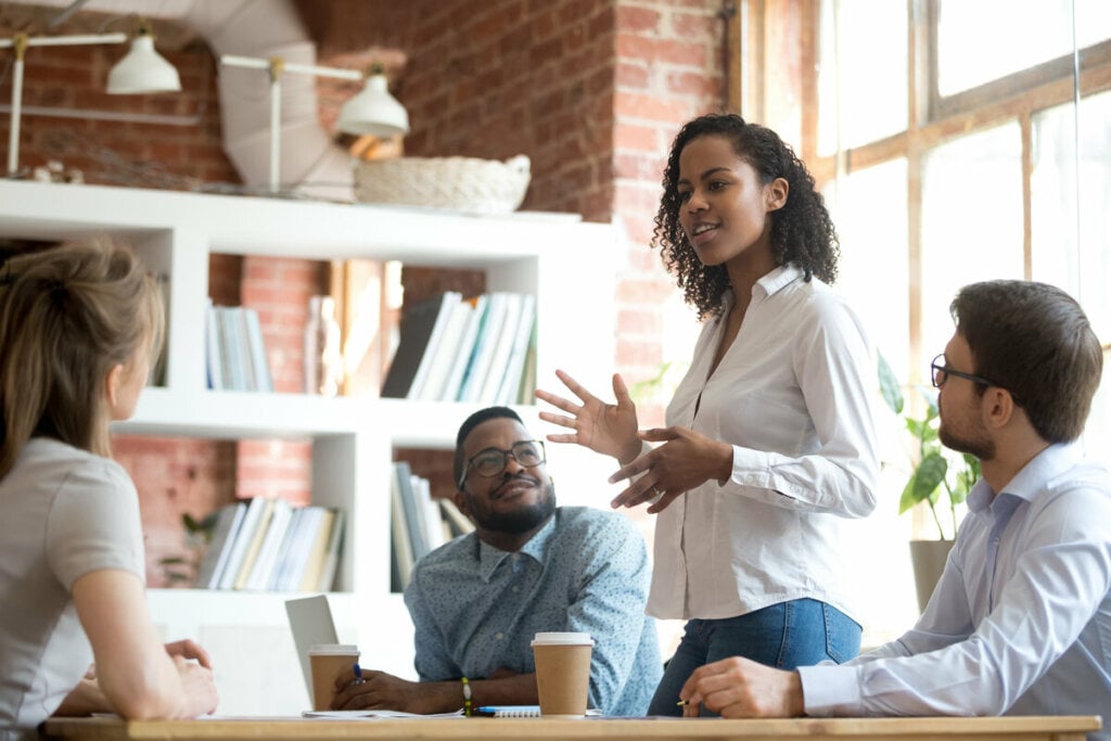 Mulher em pé em uma sala de reunião falando com pessoas