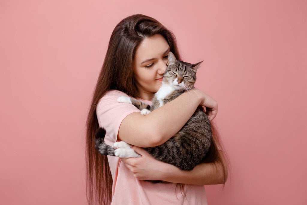 Mulher segurando gato no colo em fundo rosa