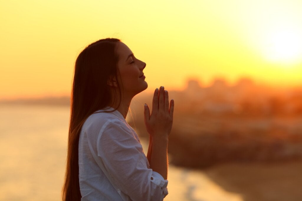 Mulher ao por do sol usando uma camisa branca, orando de olhos fechados