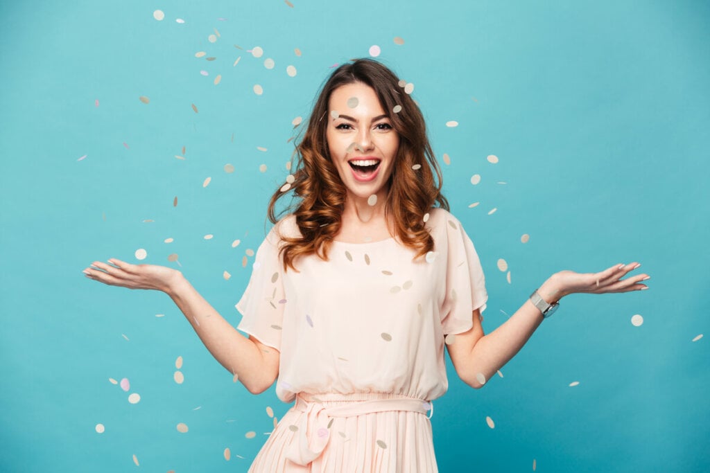 Mulher com vestido branco sorrindo com confete dourado caindo