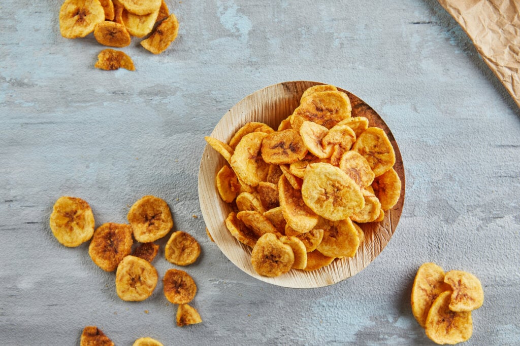 Chips de banana dentro do bowl de madeira e espalhados ao redor