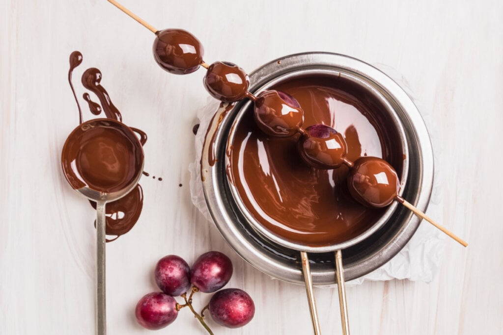 Espetinho de uvas com chocolate apoiado em recipiente com chocolate derretido