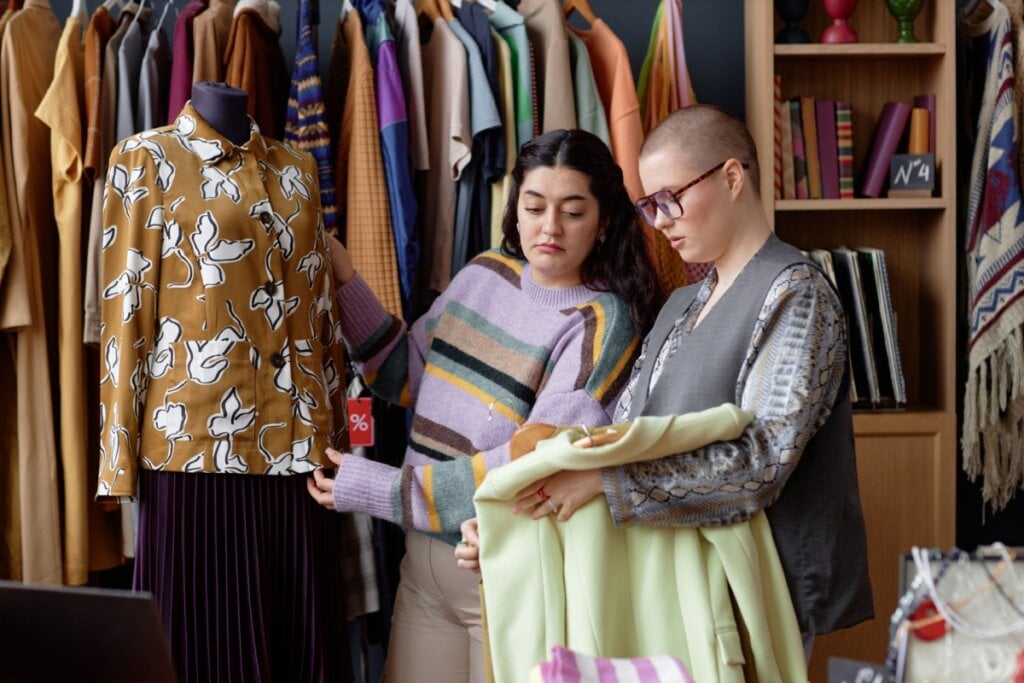 duas mulheres em espaço com diversas roupas coloridas e olhando e segurando peças