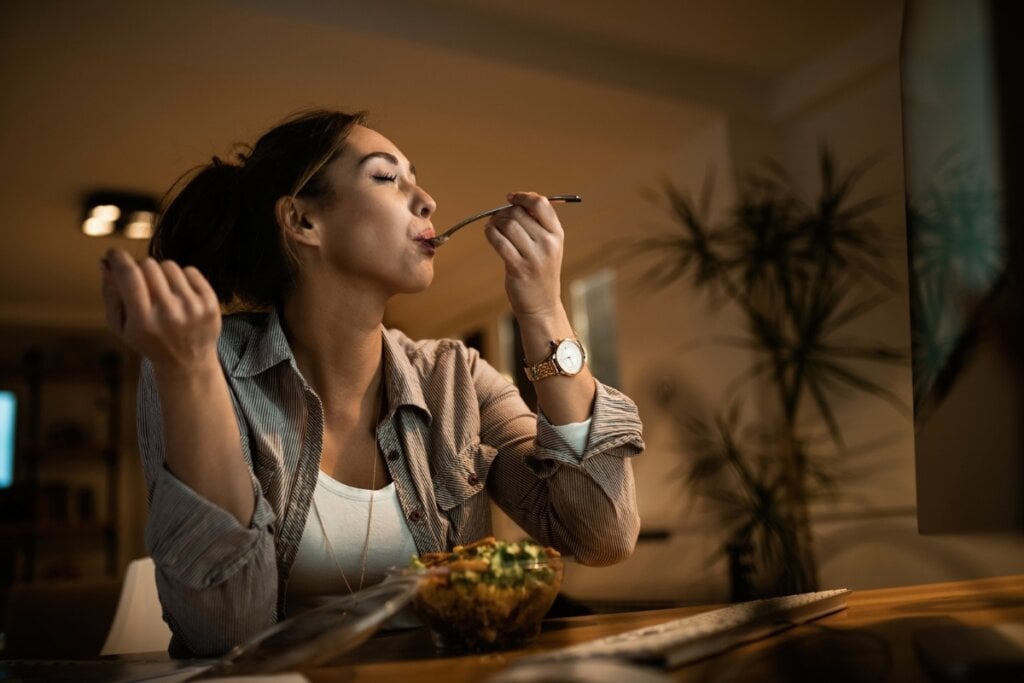 Mulher sentada em uma sala de estar a noite comendo salada 