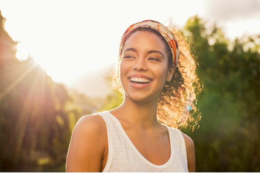 Mulher usando uma faixa de cabelo estampada e blusa branca ao ar livre sorrindo 