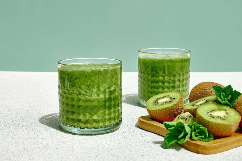 Dois copos de vidro com suco de kiwi com couve, laranja e gengibre