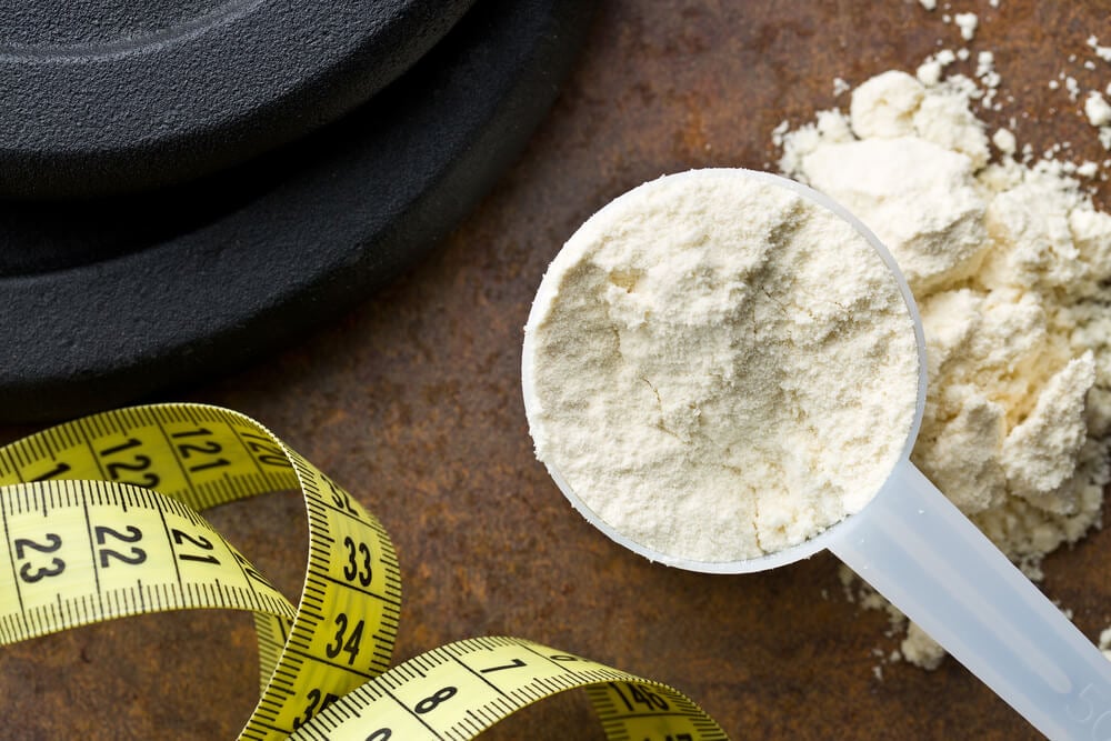 Suplemento Whey Protein, fita métrica e alteres em um balcão de granito