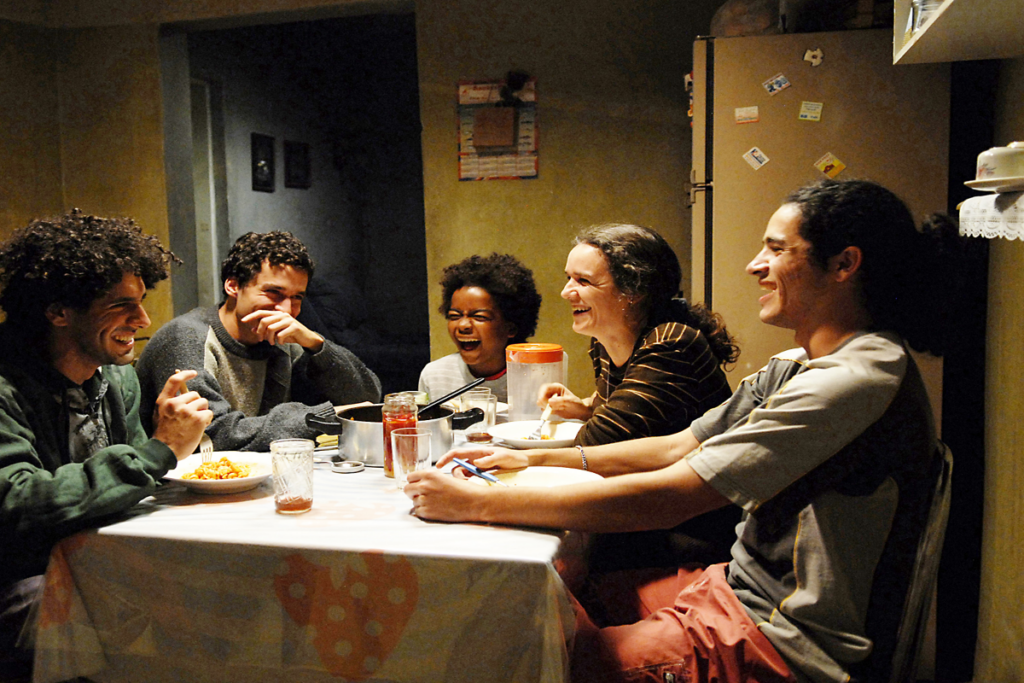 Familia sentada a mesa fazendo refeição, na imagem há 3 homens, um menino e uma mulher