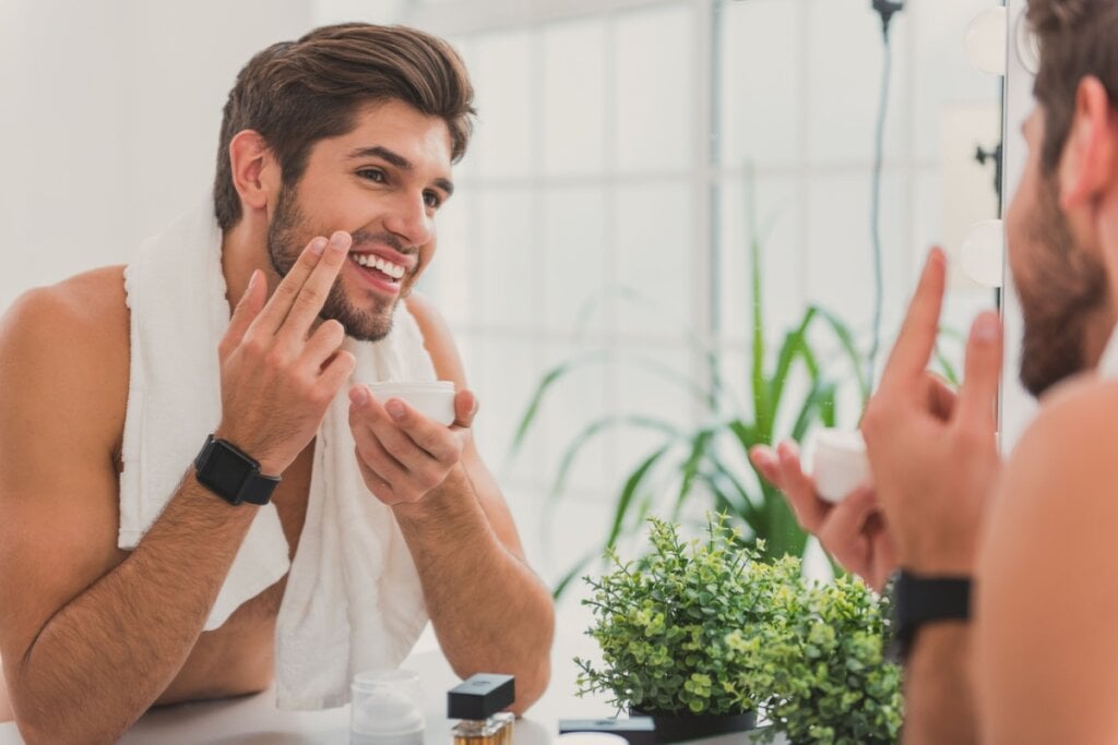 Homem em frente ao espelho passando creme hidratante na barba