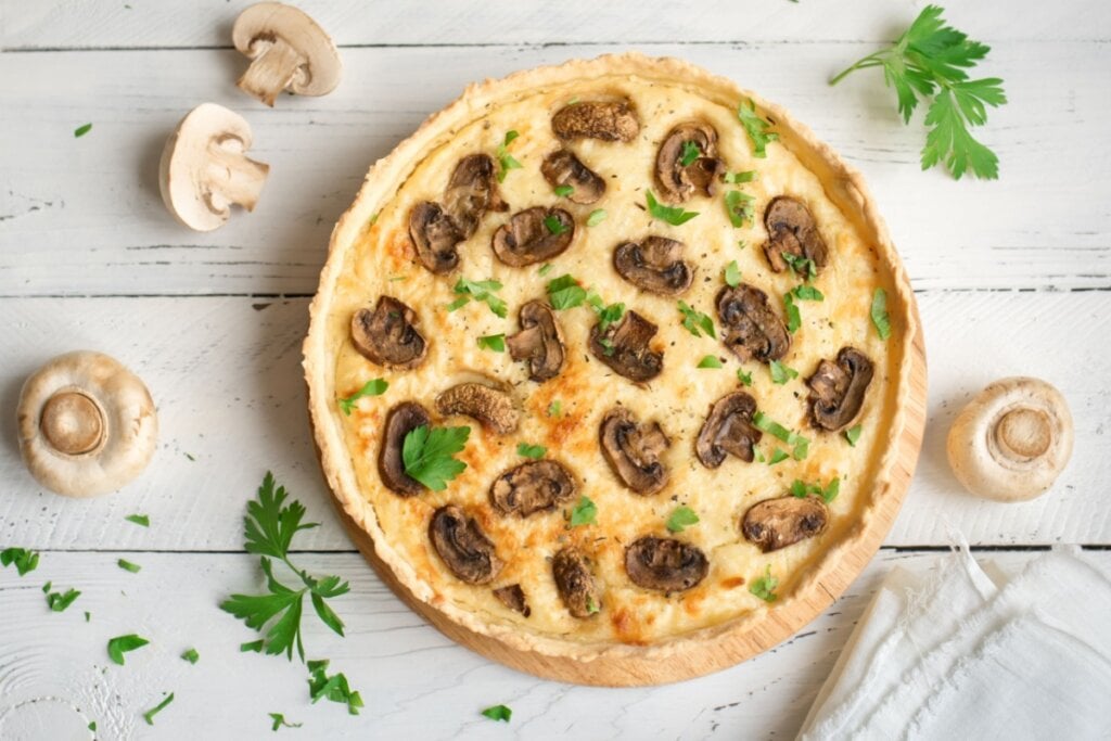 quiche de cogumelo redonda em superfície de madeira com cogumelos em volta