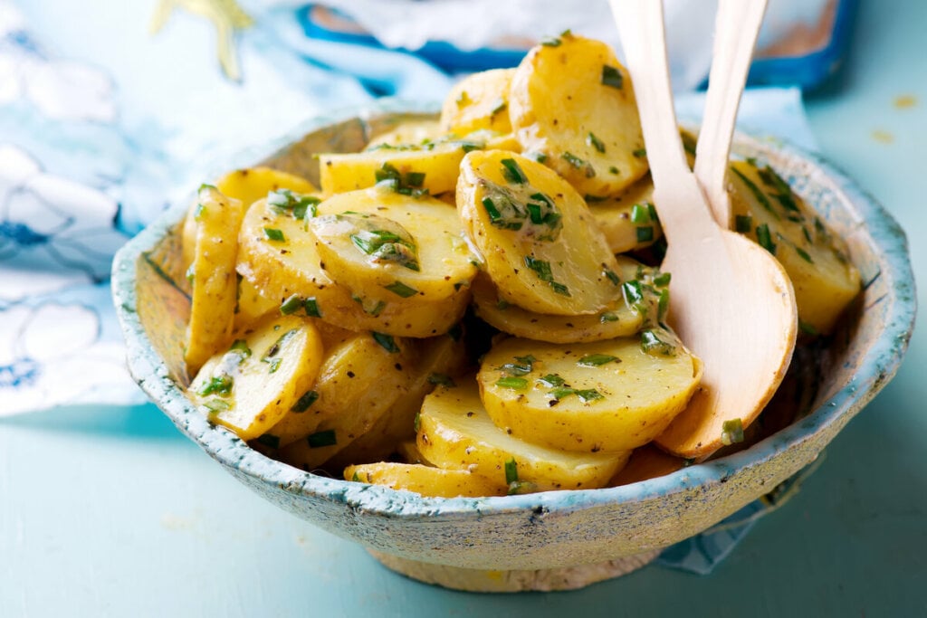 Recipiente branco com salada de batata polvilhada com salsinha picada