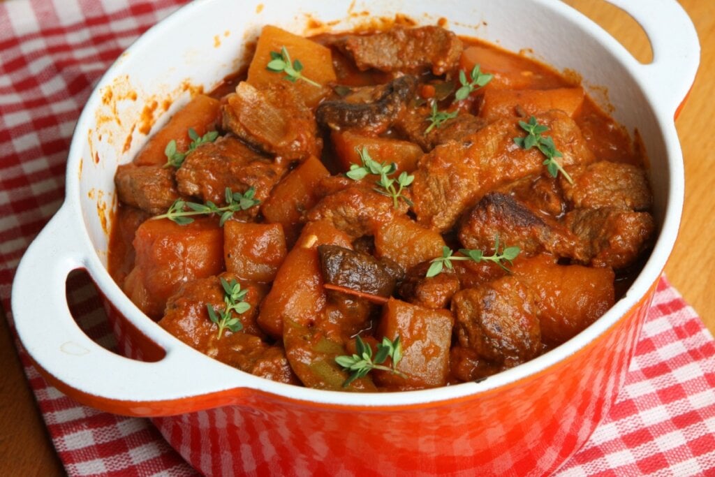 Carne refogada com mandioca, cenoura e tomilho em uma panela branca e laranja 