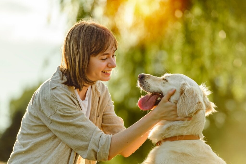 Mulher sorrindo segurando o rosto de um cachorro feliz 