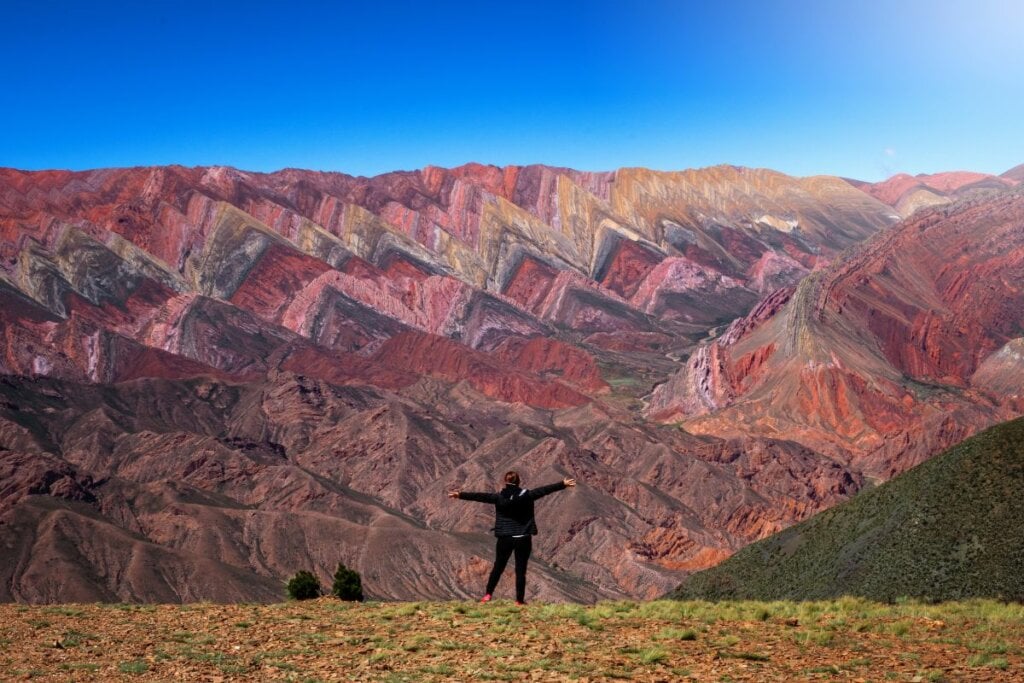 Mulher de frente para a Colina das Sete Cores, na Argentina, com os braços abertos 