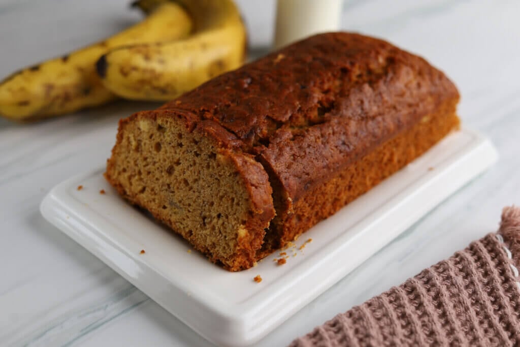 Bolo de banana em cima de um recipiente branco com bananas ao lado