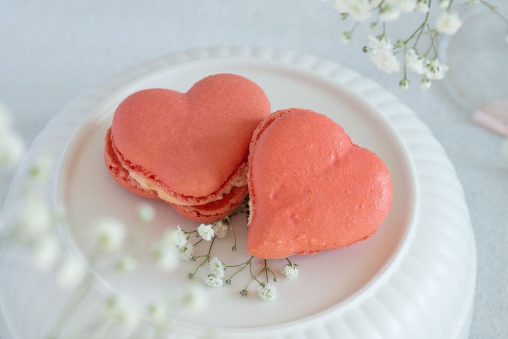 Macarons de morango em formato de coração servido em cima de pote branco de porcelana