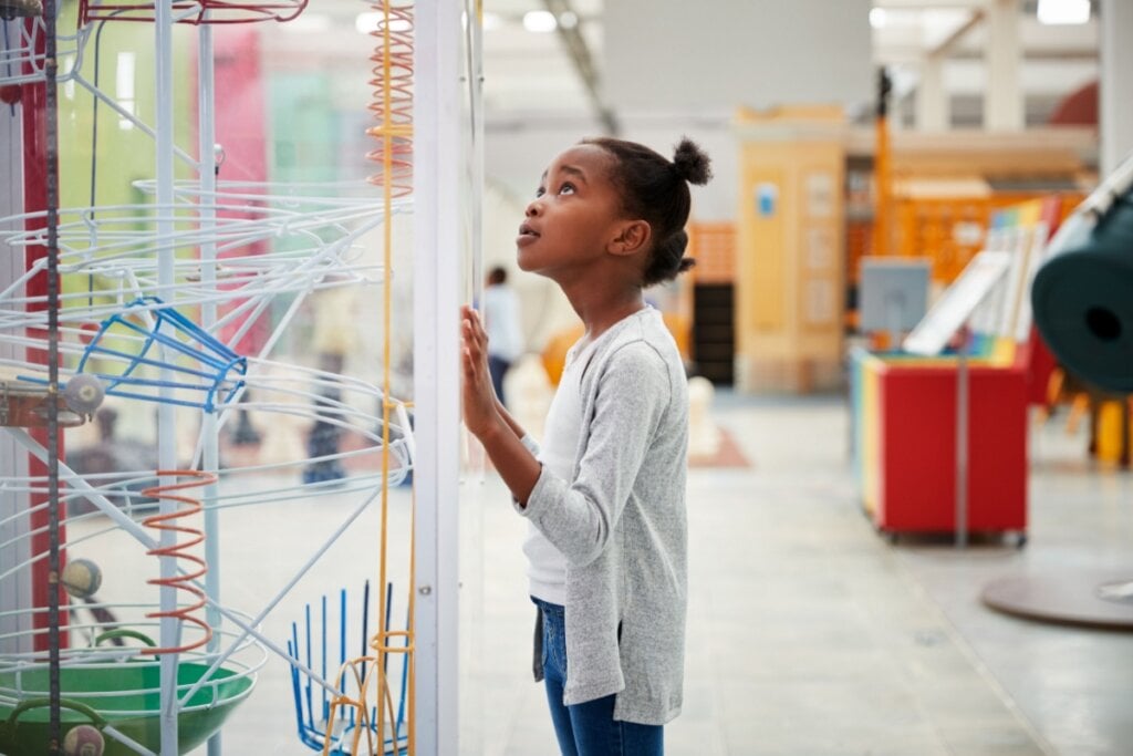 menina pequena em museu, com a mãe em vidro de peça e olhando para cima