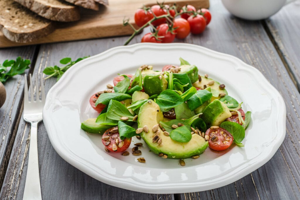 Prato branco com folhas de espinafre, pedaços de abacate, tomate e amendoim