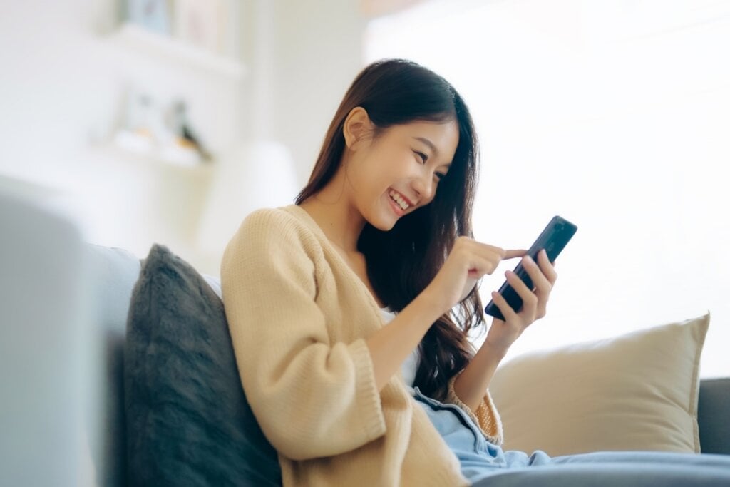 Mulher sentada sorrindo e mexendo no celular