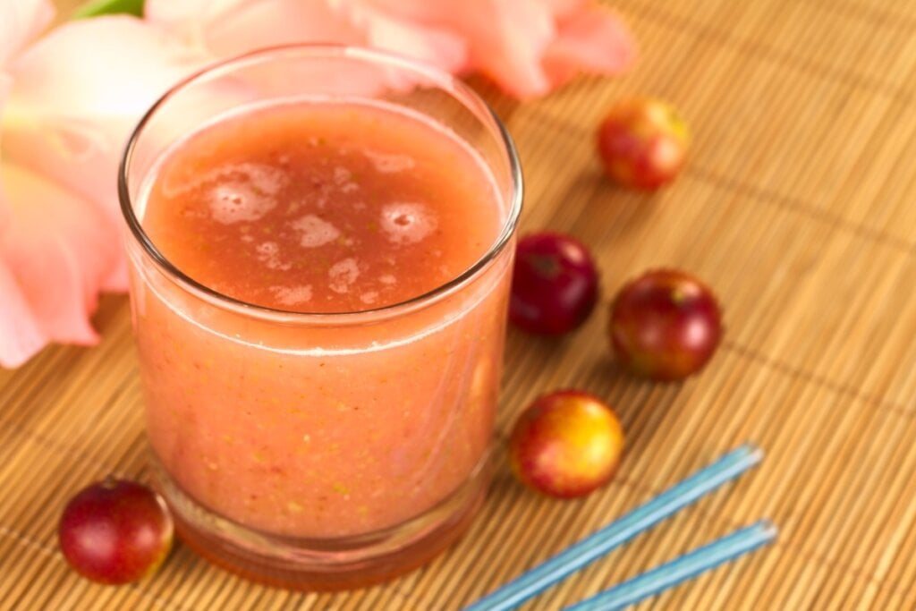 copo de vidro com suco laranja de camu-camu com frutas de camu-camu em volta e flor ao fundo