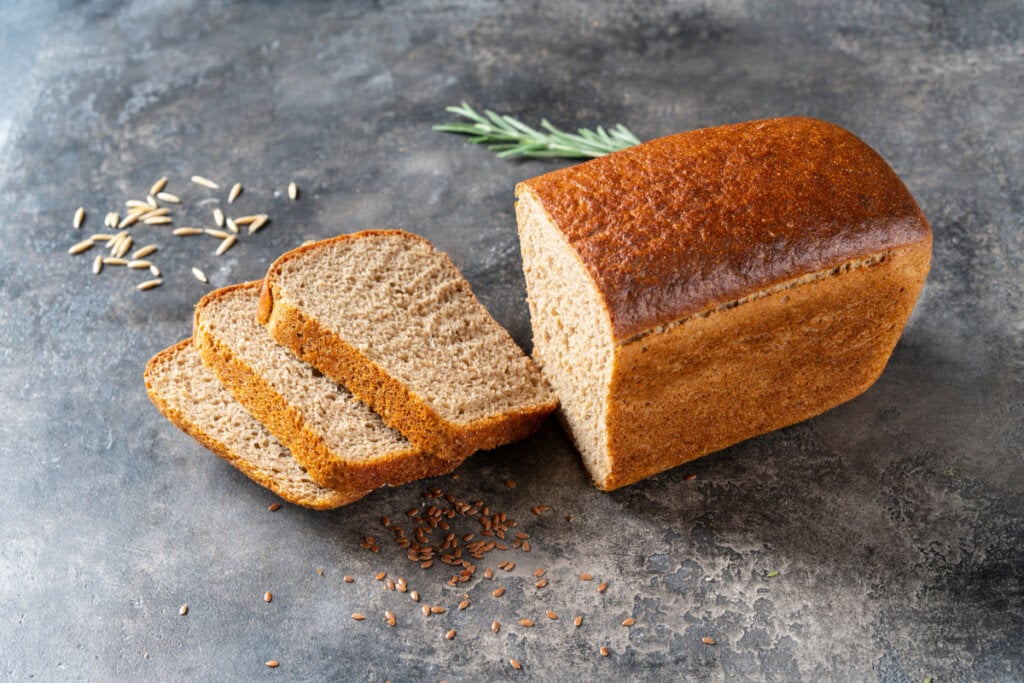 Pão marrom com três fatias ao lado em cima de superfície cinza