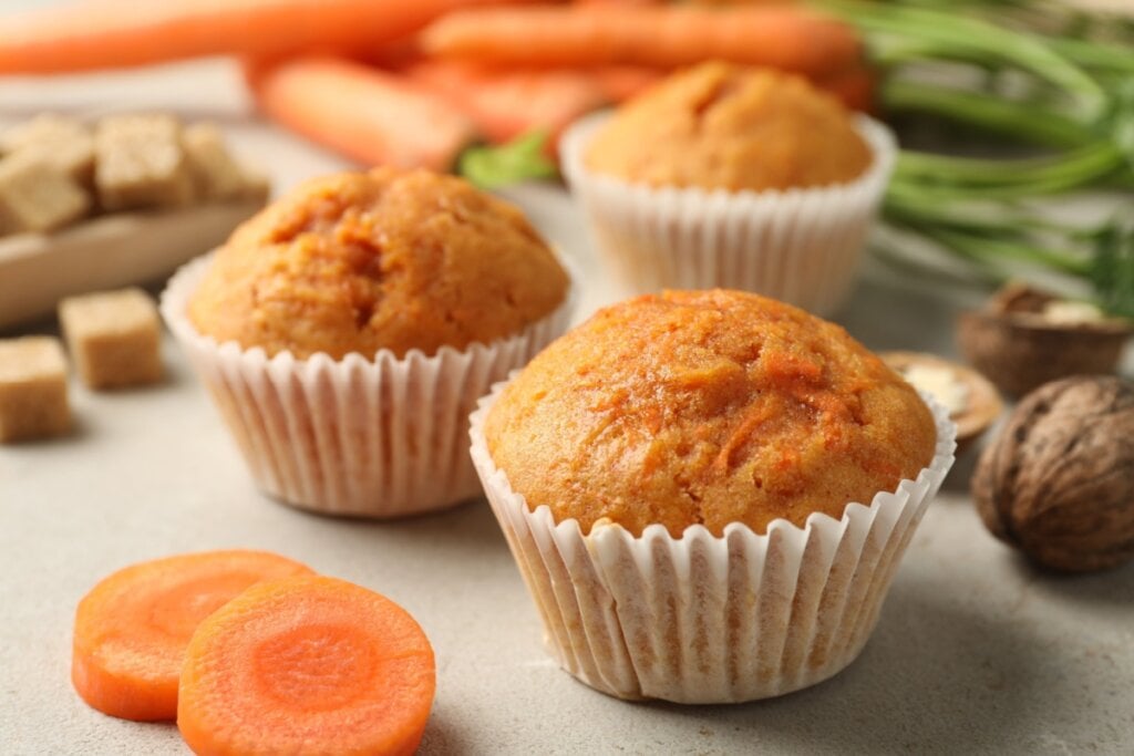 Três cupcakes de cenoura em cima de uma mesa branca com cenouras 