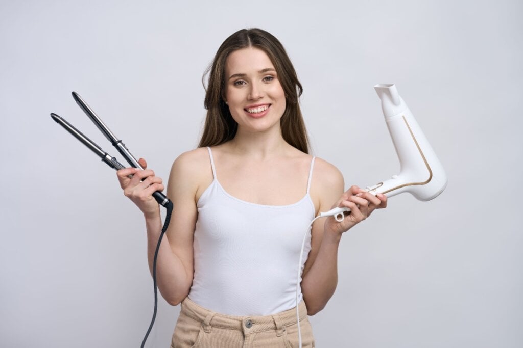 Mulher sorridente segurando um secador de cabelo branco e uma chapinha preta