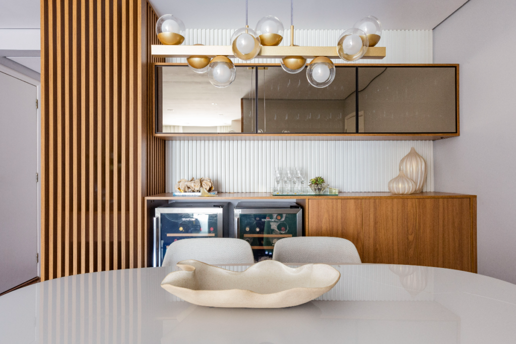 4 inspirações para inserir o buffet no design de interiores 16 Parede com buffet em madeira integrado com adega e na parte de cima uma cristaleira com portas de vidro em frente uma mesa de mármore e cadeiras brancas