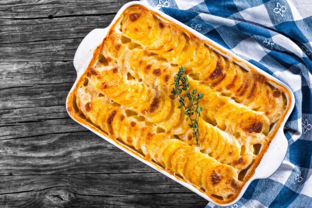8 receitas fáceis para o almoço de Dia das Mães 6 Batata gratinada em travessa com pano azul e branco ao lado