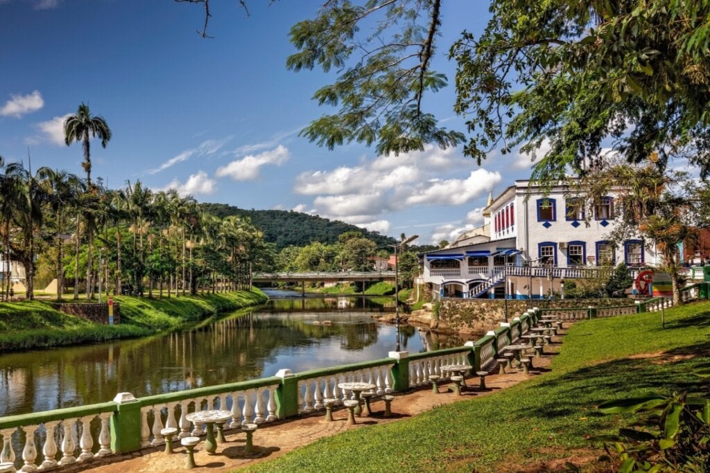 Conheça o passeio deslumbrante de Curitiba à Morretes 12 Imagem de um lago com mesinhas e banquinhos de pedra ao redor, ao fundo um prédio histórico em branco e azul, cercado por arvores