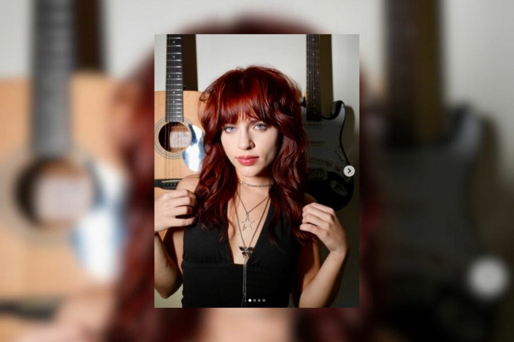 3 cores de cabelo ideais para o inverno 12 Mulher com cabelo ruivo com franja e usando uma blusa preta posando para foto